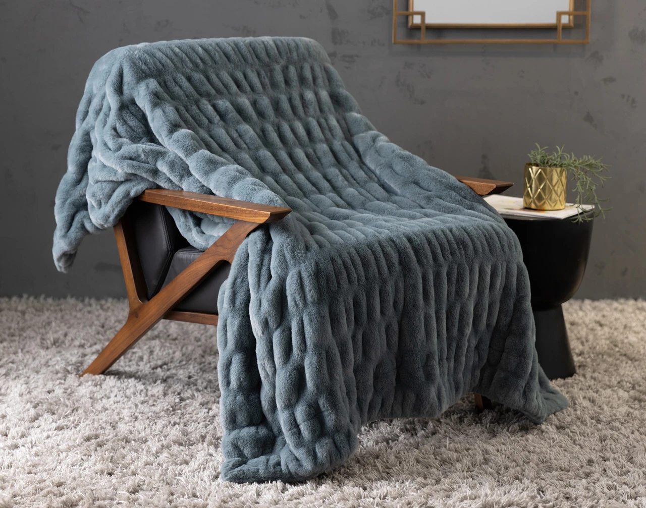 Our Cocoon Plush Throw in Juniper draped over a chair in a grey room.