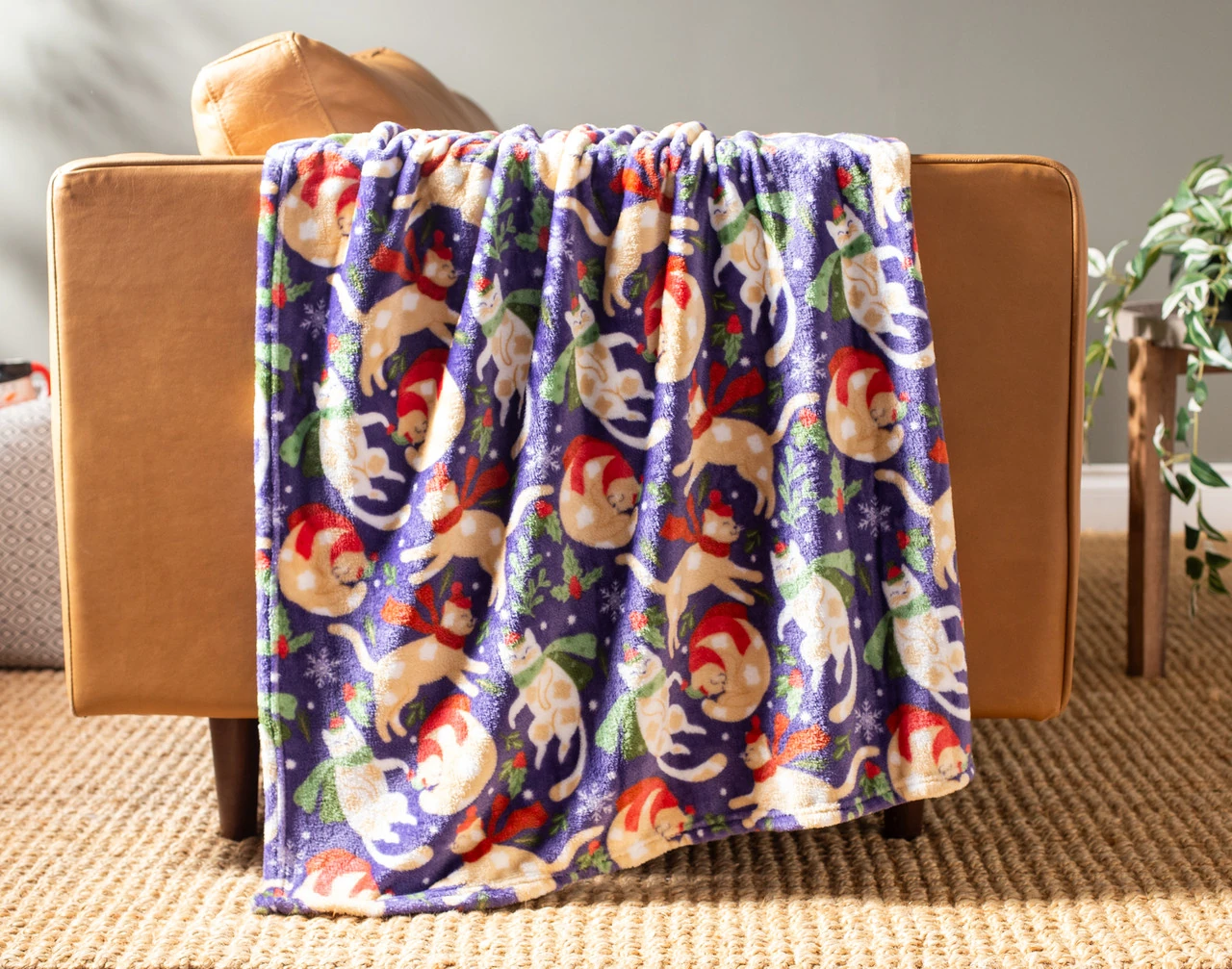 Our Holiday Fleece Throw - Festive Felines draped over a brown couch.