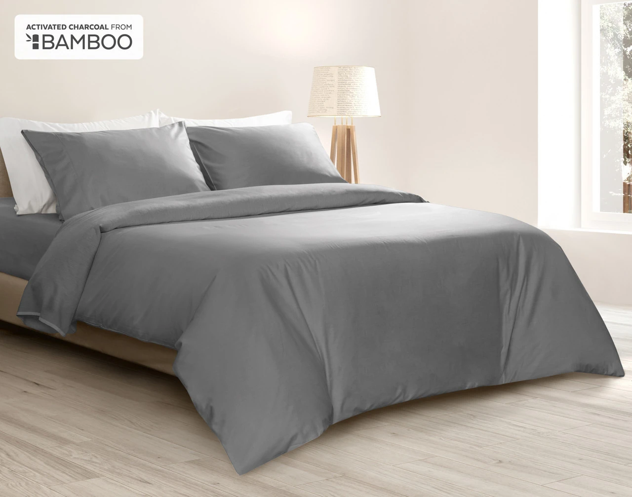 Angled view of our Deep Charcoal Bamboo Cotton Duvet Cover Set dressed over a queen bed in a bright bedroom.