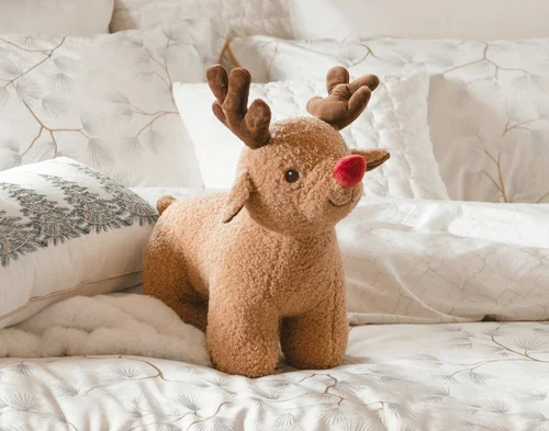 Our Rudolph Holiday Cushion resting on a holiday-ready bed.