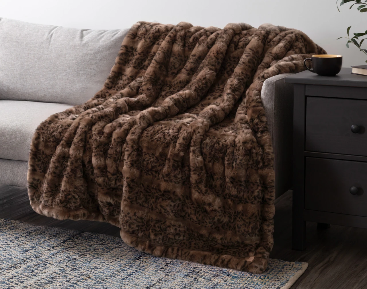 Our Bubble Faux Fur Throw in Sable draped over a grey couch.