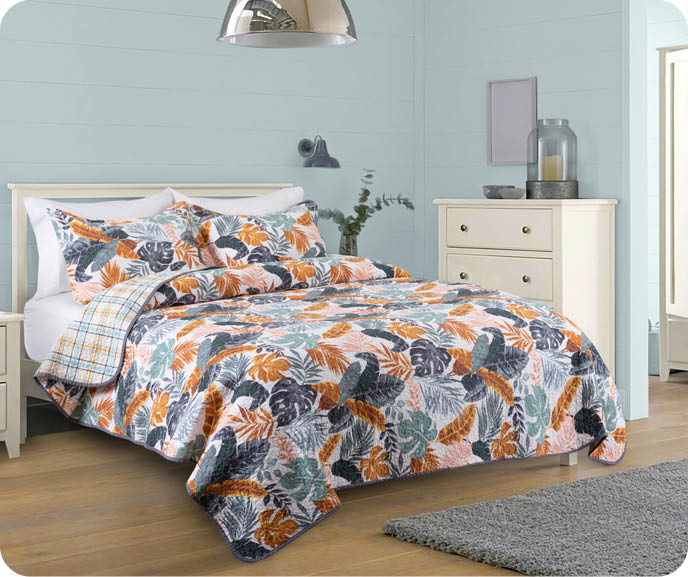 Our Tropics Cotton Quilt Set features a reversible design with a tropical multicoloured leaf print and coordinating plaid on its reverse. Pictured on a bed with its matching pillow shams.