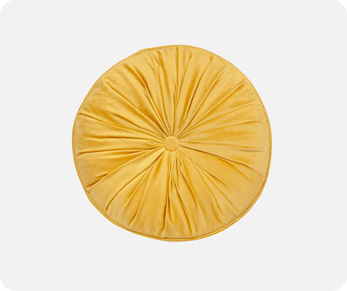 Our Round Corduroy Cushion in Gold features a yellow velvet surface and ruched construction fastened with a decorative button on both sides. Pictured on a white background.