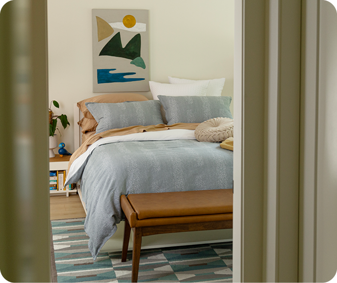 The Aquatico Duvet Cover in blue with a frothy water pattern dressing a bed with brown-orange sheets, a multicoloured throw blanket, a cream throw cushion, and white square cushions. The Aquatico Duvet Cover in blue with a frothy water pattern dressing a bed with brown-orange sheets, a multicoloured throw blanket, a cream throw cushion, and white square cushions.