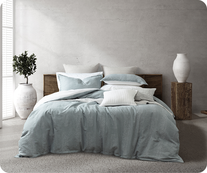 The Aquatico Duvet Cover in blue with a frothy water pattern with white cushions and white sheets on a queen bed in a grey bedroom. The Aquatico Duvet Cover in blue with a frothy water pattern with white cushions and white sheets on a queen bed in a grey bedroom.