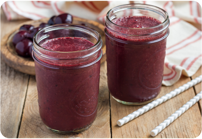 Angled view of two cherry smoothies sitting on a wooden table in glass cups. Angled view of two cherry smoothies sitting on a wooden table in glass cups.