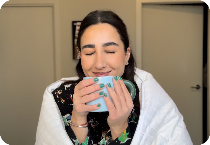 Woman drinking a warm cup of coffee under a duvet.