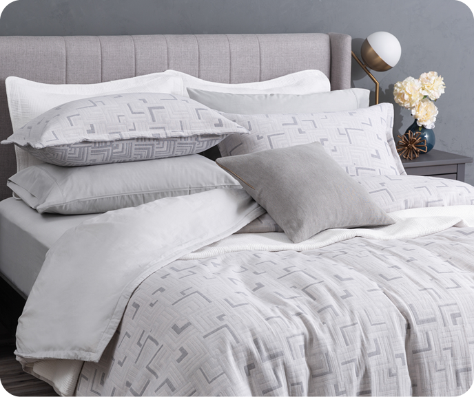 The geometric silver Centro Duvet Cover from the Portugal Reserve Collection with its matching pillow shams dressing a grey bed with white sheets. The geometric silver Centro Duvet Cover from the Portugal Reserve Collection with its matching pillow shams dressing a grey bed with white sheets.