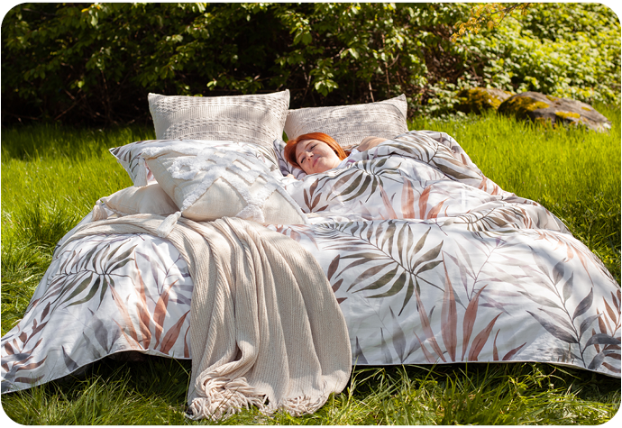 Red-haired woman sleeping in a fully dressed bed in a green meadow, with warm sunlight beaming down on her.