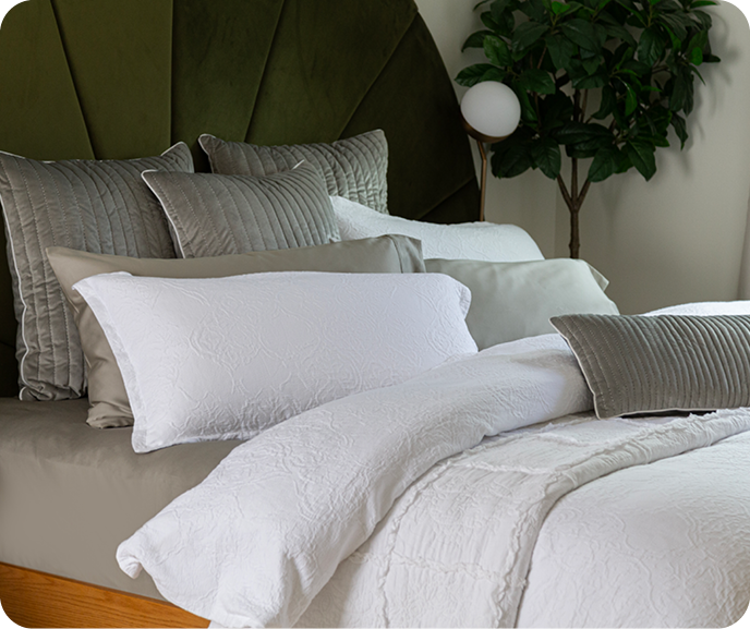 The Portugal Reserve Collection's white Corinthia Duvet Cover and matching pillow sham paired on a bed with sheets and cushions in different green hues. The Portugal Reserve Collection's white Corinthia Duvet Cover and matching pillow sham paired on a bed with sheets and cushions in different green hues.
