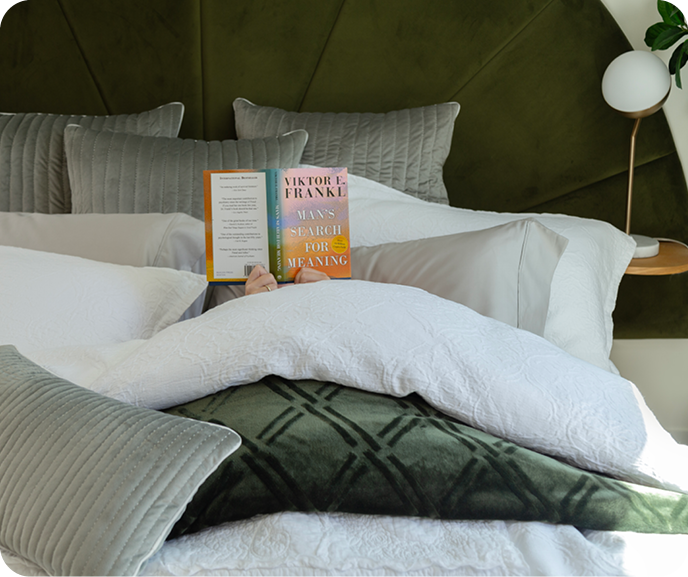 Someone reading in a bed dressed in the Portugal Reserve Collection's white Corinthia Duvet Cover, matching pillow shams, and green cushions. Someone reading in a bed dressed in the Portugal Reserve Collection's white Corinthia Duvet Cover, matching pillow shams, and green cushions.