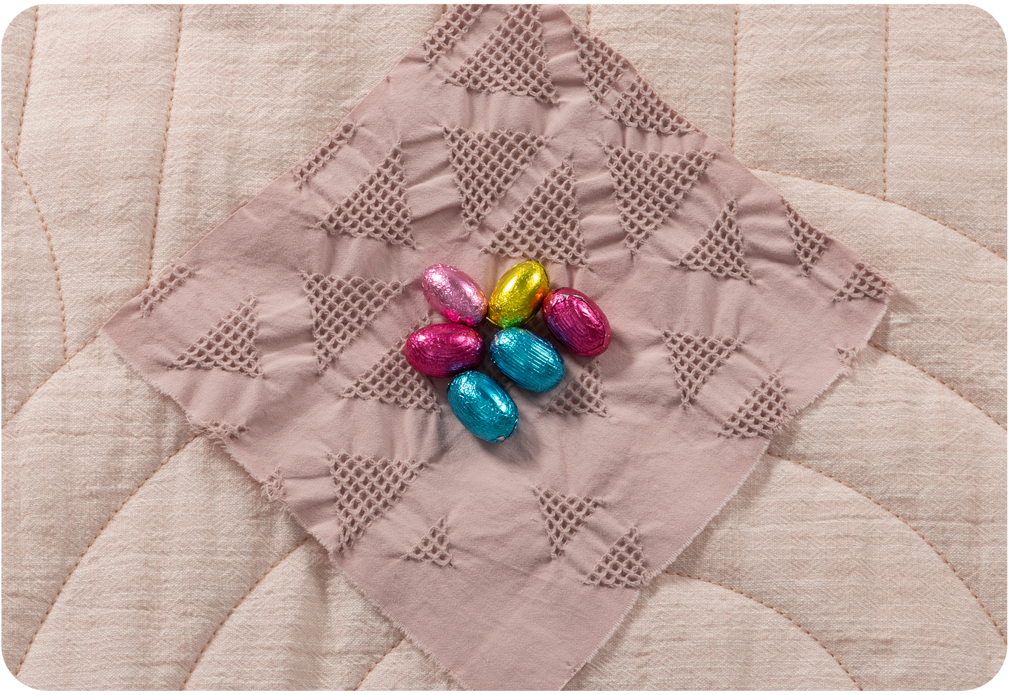 Chocolate eggs in bright pastel coloured wrappers in the centre of a diamond of fabric.