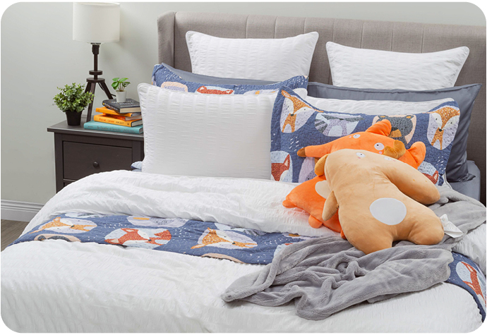 Our Kailua Bedding Collection and Forest Friends Cotton Quilt Set styled on a bed with a Fleece Throw and Cuddle Cushions.