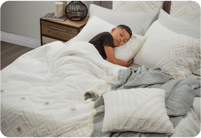 A boy sleeps on a bed styled with our Charity Bedding Collection and Cozumel Muslin Blanket.