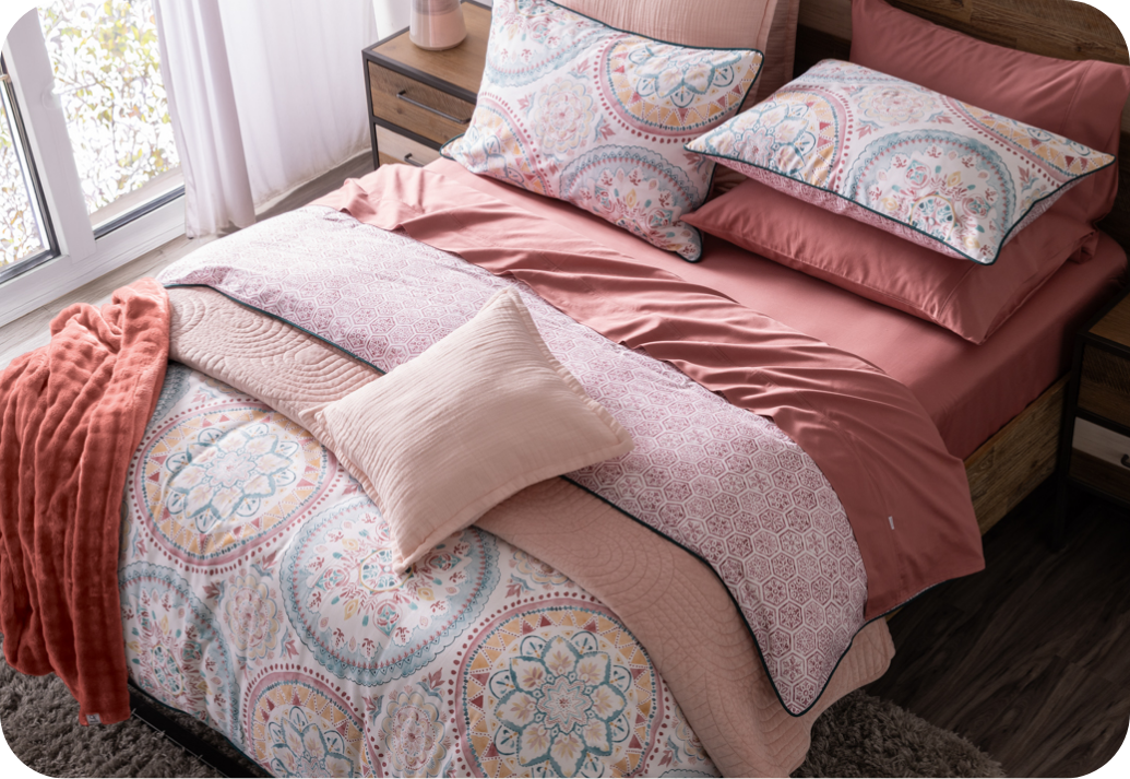 A QE Home quilt folded at the base of a bed.