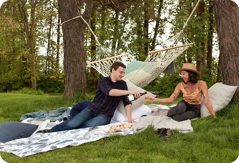 Two people sitting at a hammock picnic set up on the grass.
