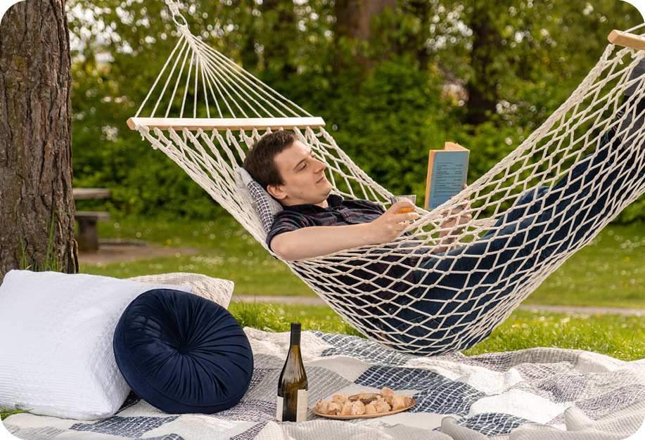 A person lounging in a hammock reading a book surrounded by QE Home bedding and accessories.
