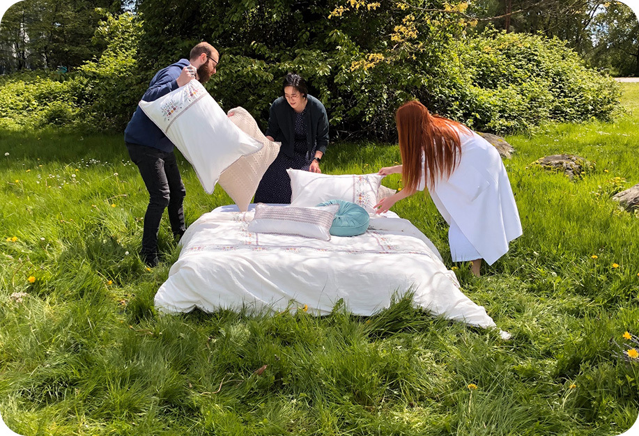 Three people dressing a bed with Kaysa Collection and assorted QE Home cushions .