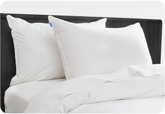 Two Luxurious Down Pillows laying on a bed against a dark bed frame.