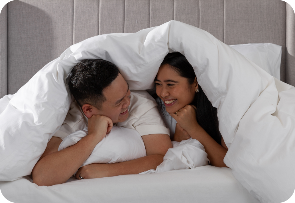 Couple smiling at each other under a duvet.