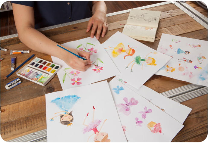A woman is shown painting colourful illustrations on white paper.