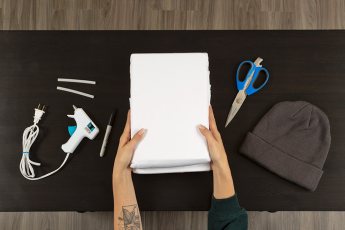 Top view of a glue gun, scissors, white sheet, and toque over a black table.