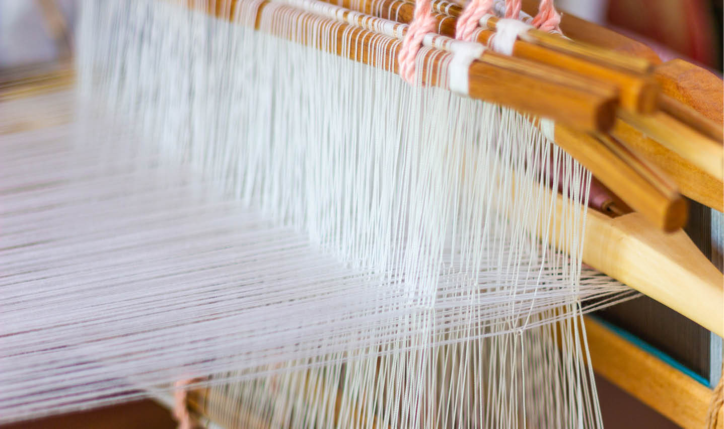 Close-up of silk threads being spread and weaved on a wooden loom. Close-up of silk threads being spread and weaved on a wooden loom.