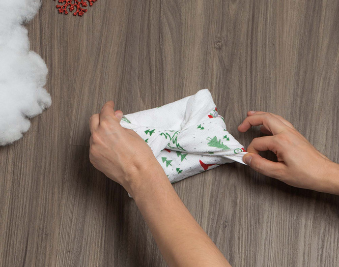 Two hands tying the top of a small fabric tea towel gift wrap together.