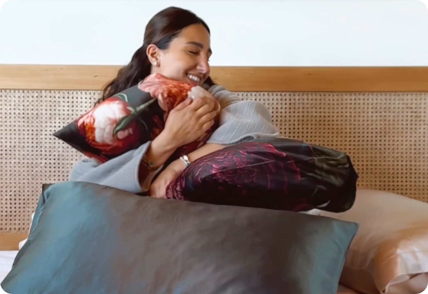 Woman on a bed hugging some pillows.
